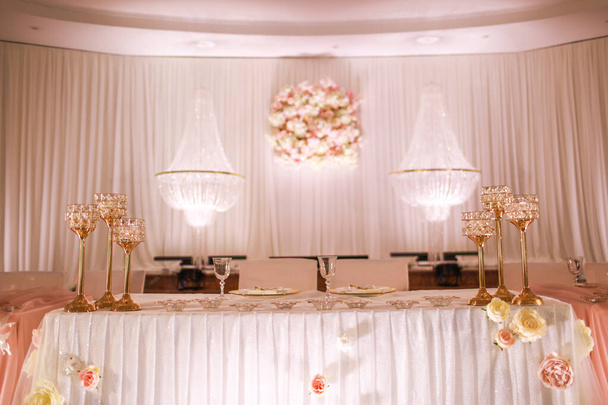 świąteczna ozdoba stołu weselnego z kryształowymi żyrandolami, złotymi świecznikami, świecami i białymi różowymi kwiatami. stylowy dzień ślubu. - Zdjęcie, obraz
