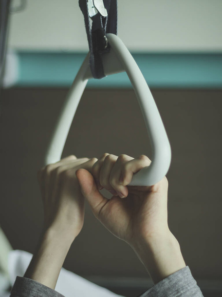 Caucasian guy patient hold with both hands on a triangular therapeutic arc with a gripper installed above the bed in the hospital ward, close-up side view.Concept of trauma devices for bedridden patients. - Foto, imagen