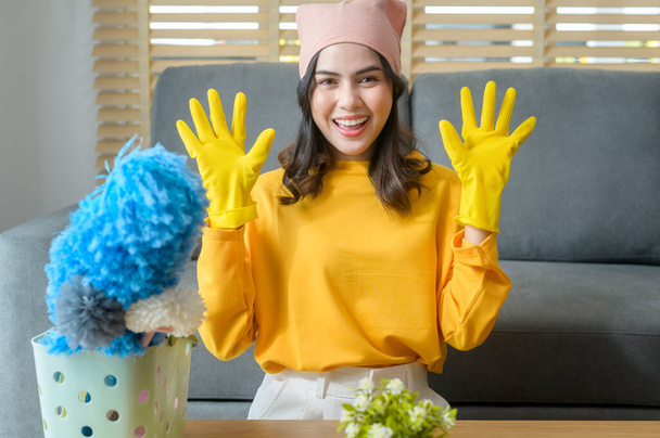Une jeune femme heureuse portant des gants jaunes et tenant un panier de fournitures de nettoyage dans le salon. - Photo, image