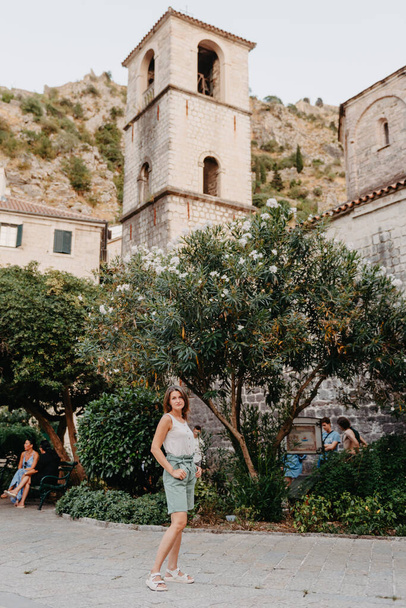 Girl Tourist Resting in the Ancient Narrow Street On A Beautiful Summer Day In MEDITERRANEAN MEDIEVAL CITY, OLD TOWN KOTOR, MONTENEGRO. Young Beautiful Cheerful Woman Walking On Old Street - Foto, immagini