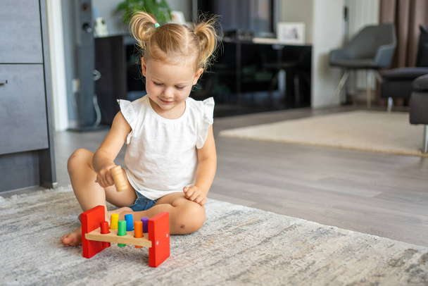 Cute caucasian little girl playing on the floor at home with eco wooden toys. Montessori toy. The child playing educational games. High quality photo - Fotó, kép