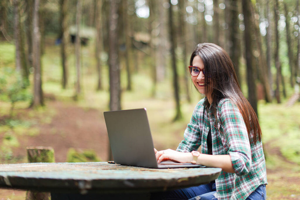 Young latin woman sitting in the forest working with laptop freelancing looking camera smiling at Costa Rica. High quality photo - Photo, Image