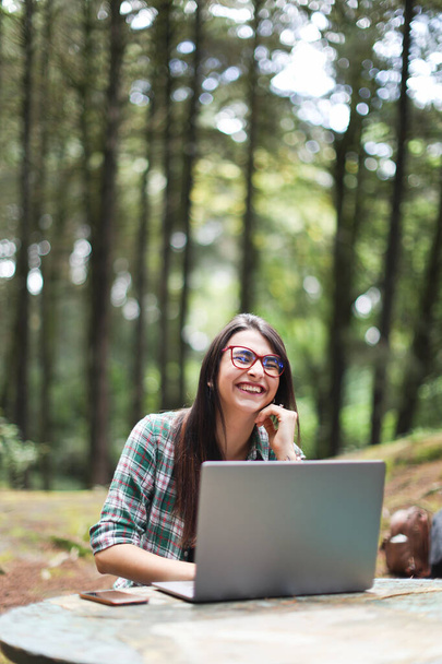 Egy fiatal latin nő ül az erdőben, laptoppal dolgozik, szabadúszó mosollyal Costa Ricán. Kiváló minőségű fénykép - Fotó, kép