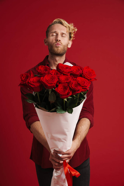 White bearded man making kiss lips while posing with roses isolated over red wall - Fotoğraf, Görsel