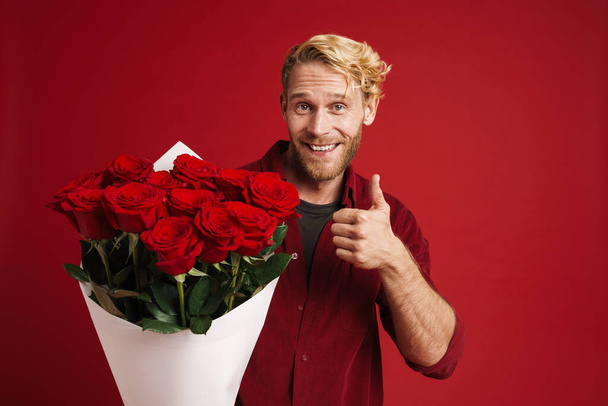 White bearded man showing thumb up while posing with roses isolated over red wall - Foto, Imagem