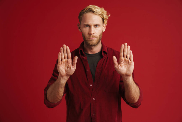 White bearded man wearing shirt showing stop gesture at camera isolated over red wall - Foto, afbeelding