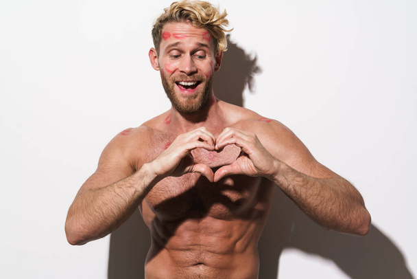 Shirtless blonde man with lipstick smudge showing heart gesture isolated over white background - Zdjęcie, obraz