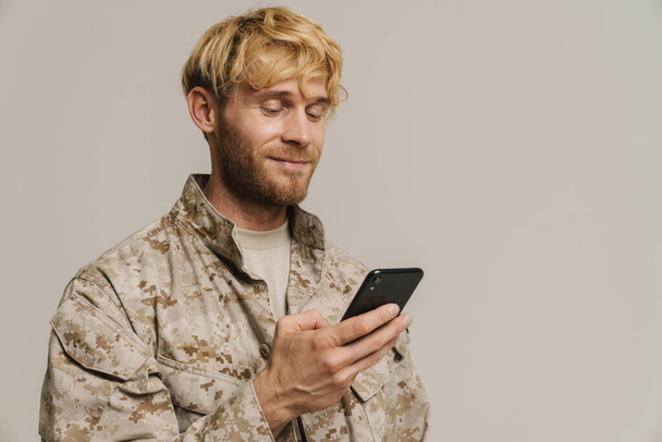 White military man wearing uniform smiling and using cellphone isolated over white wall - Valokuva, kuva