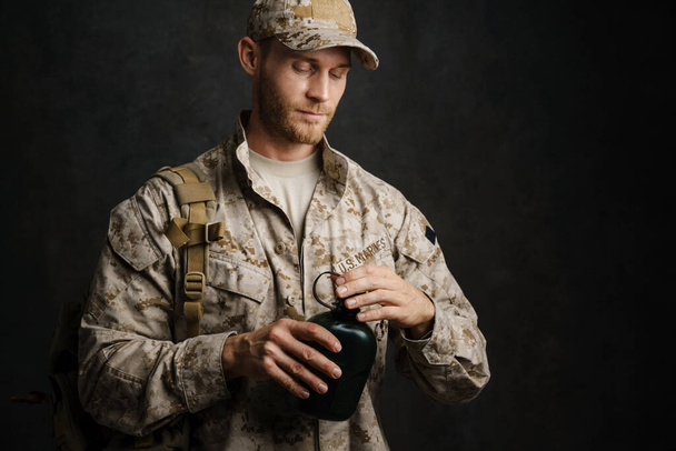 White military man wearing uniform posing with flask and backpack isolated over black wall - Φωτογραφία, εικόνα