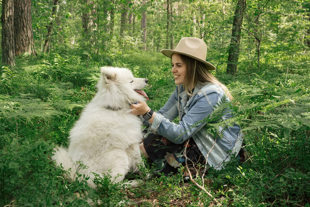 Young beautiful woman spending time with her white fluffy dog samoyed in the forest - Foto, Imagen
