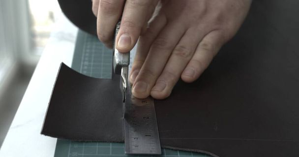 Working process of crafting a new handmade leather wallet in the leather workshop. Mans hands working with knife and iron ruler and cutting a leather - Photo, image