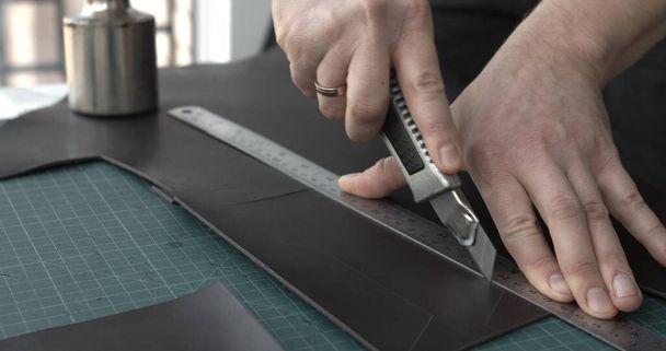 Working process of crafting a new handmade leather wallet in the leather workshop. Mans hands working with knife and iron ruler - Photo, image