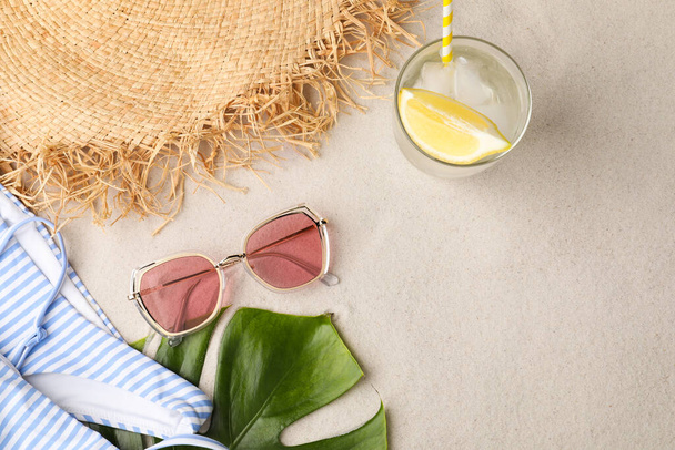 Stylish sunglasses, glass of refreshing drink and beach accessories on sand, flat lay - Foto, Imagem