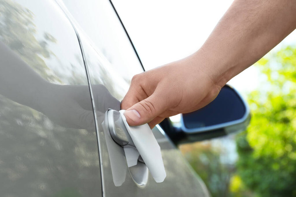 Man with napkin sanitizing car door handle outdoors, closeup - Foto, immagini