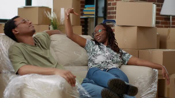 Африканцы чувствуют себя уставшими от переезда в новый дом, делая перерыв от распаковки мебели в квартире. Покупка первой недвижимости по ипотечному кредиту. Портативный выстрел. - Кадры, видео