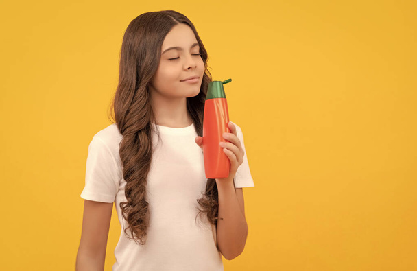 smiling teen girl with long hair smelling shampoo bottle, beauty. - Photo, Image