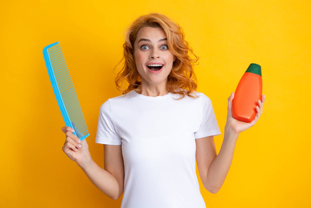 Redhead woman with a comb, isolated on yellow background. Woman hold bottle shampoo and conditioner - Foto, Imagen