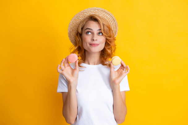 Joven mujer complacida aislada sobre fondo amarillo comiendo macarrones. Chica comer macarrones franceses - Foto, Imagen