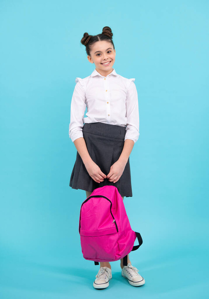 Zpátky do školy. Teenager školačka ve školní uniformě s taškou. Školní děti na modrém izolovaném pozadí studia. Šťastný teenager, pozitivní a usměvavé emoce dospívající školačky - Fotografie, Obrázek