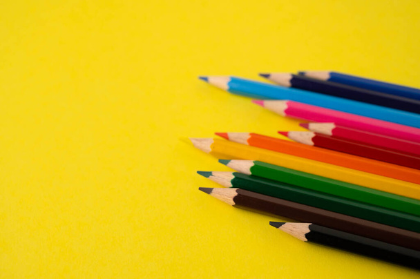 A row of unevenly arranged colored pencils on a yellow background with copy space. - 写真・画像