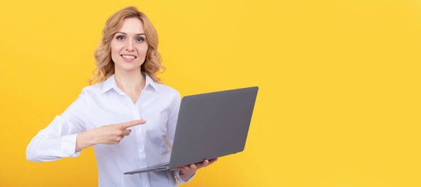 vrolijke ondernemer dame in wit shirt wijzend vinger op laptop op gele achtergrond, presentatie. Vrouw geïsoleerd gezicht portret, banner met mock up kopieerruimte - Foto, afbeelding