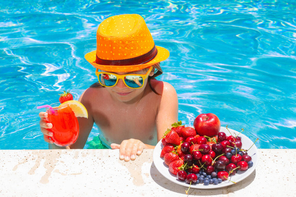 Little child by the pool eating fruit and drinking lemonade cocktail. Summer kids vacation concept - Foto, Imagem