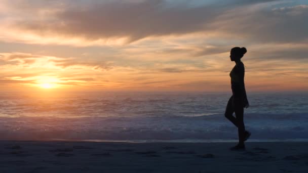 Active athlete silhouette keeping fit for healthy lifestyle, doing stretch exercises after running on beach front of ocean. Sporty female jogger warm up before workout with view of sea and sunset - Záběry, video