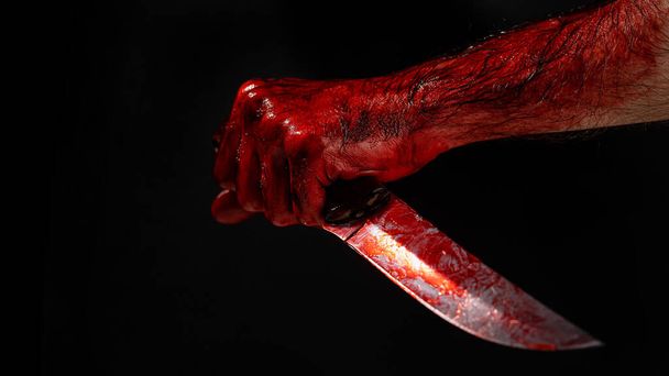 Man holding knife with bloody hand on black background - Foto, imagen