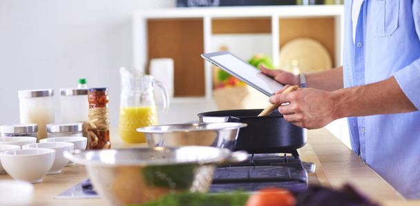 Man following recipe on digital tablet and cooking tasty and healthy food in kitchen at home. - Fotoğraf, Görsel