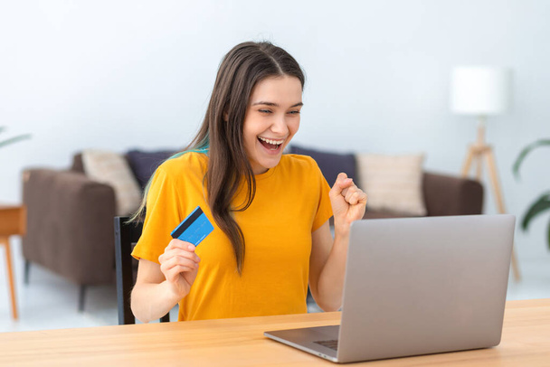 Portrait of pleasantly excited Caucasian woman shopping online, using laptop. Happy smiling female holding credit card looking at the computer screen - Fotoğraf, Görsel