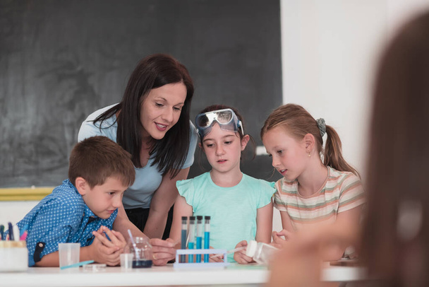 Elementary School Science Classroom: Enthusiastic Teacher Explains Chemistry to Diverse Group of Children, Little girl Mixes Chemicals in Beakers. Children Learn with Interest. Hi quality stock photo. - Valokuva, kuva
