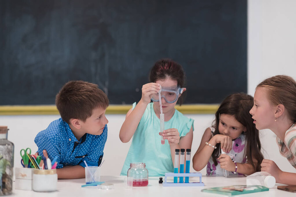 Elementary School Science Classroom: Enthusiastic Teacher Explains Chemistry to Diverse Group of Children, Little Boy Mixes Chemicals in Beakers. Children Learn with Interest. Slow motion. - Zdjęcie, obraz
