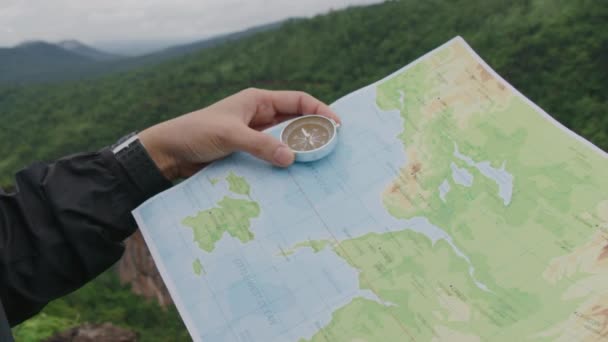 Compass and map in hands of traveler for checking and searching position and direction at the top of peak of mountain while hiking for camping - Filmati, video