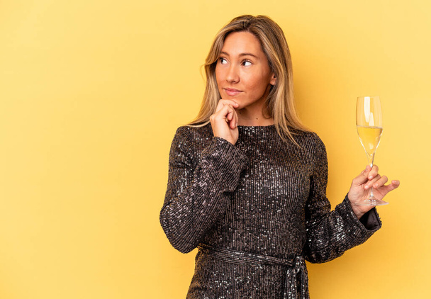 Young caucasian woman celebrating new year holding cava cup isolated on yellow background looking sideways with doubtful and skeptical expression. - Fotografie, Obrázek