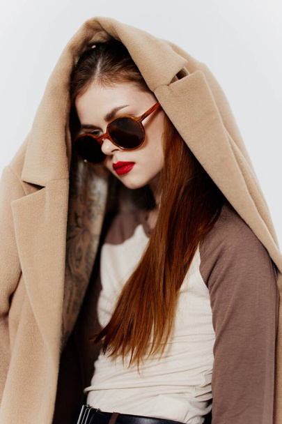 Рыжая девушка в очках и в пальто на голове отводит взгляд. Знамя модного дизайна магазина одежды. Высокое качество фото - Фото, изображение
