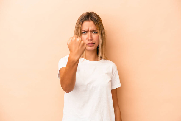 Young caucasian woman isolated on beige background showing fist to camera, aggressive facial expression. - Photo, Image