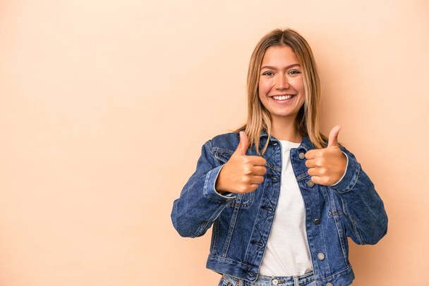 Young caucasian woman isolated on beige background smiling and raising thumb up - 写真・画像