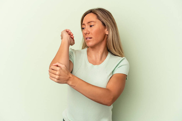 Young caucasian woman isolated on green background massaging elbow, suffering after a bad movement. - Photo, image