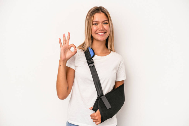 Young caucasian woman with broken hand isolated on white background cheerful and confident showing ok gesture. - Foto, afbeelding