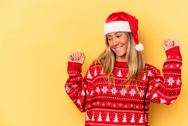 Joven mujer caucásica celebrando Navidad aislada sobre fondo amarillo levantando puño después de una victoria, concepto ganador. - Foto, Imagen
