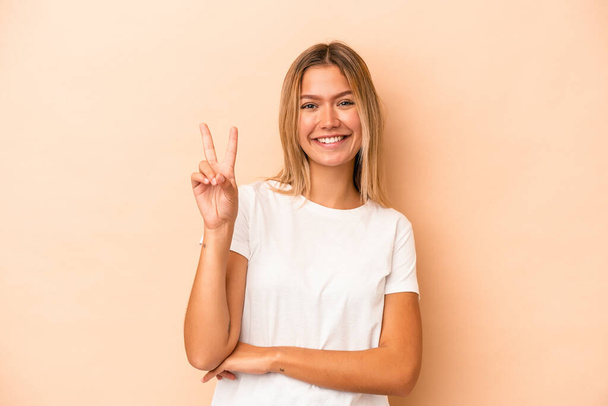 Young caucasian woman isolated on beige background showing number two with fingers. - Foto, immagini