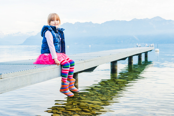 Outdoor Portret van een schattig klein meisje, zittend op een pier - Foto, afbeelding