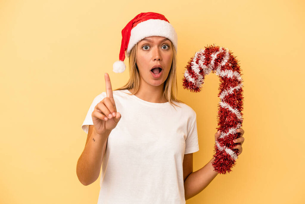 Young caucasian woman holding big christmas stick isolated on yellow background having an idea, inspiration concept. - Photo, Image