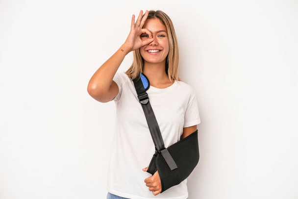 Young caucasian woman with broken hand isolated on white background excited keeping ok gesture on eye. - Fotoğraf, Görsel