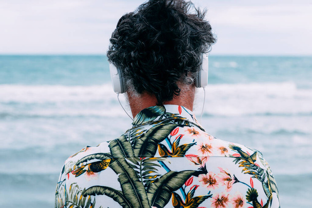 Back man zenét hallgat, miközben a tengert nézi a parton. - Fotó, kép
