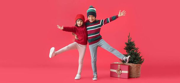 Happy little children in winter clothes, with Christmas tree and gift on red background - Foto, afbeelding