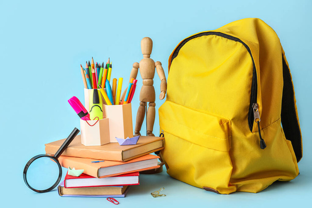 Cups with school stationery, wooden mannequin and backpack on blue background - Φωτογραφία, εικόνα