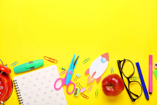 Papierraket met schoolbriefpapier, bril en appel op gele achtergrond - Foto, afbeelding