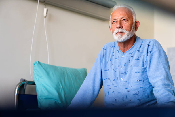 Thoughtful elderly male patient in hospital bed in ward room. Healthcare people problem concept - 写真・画像