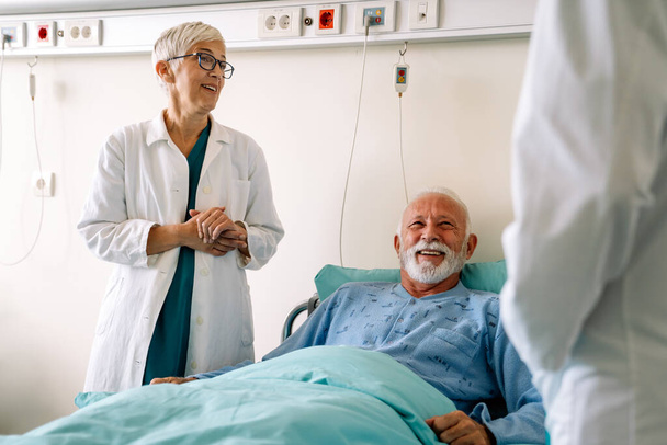 Doctor talking to senior male patient in hospital bed who is recovering from the disease. Healthcare, coronavirus, people concept. - Foto, Imagen